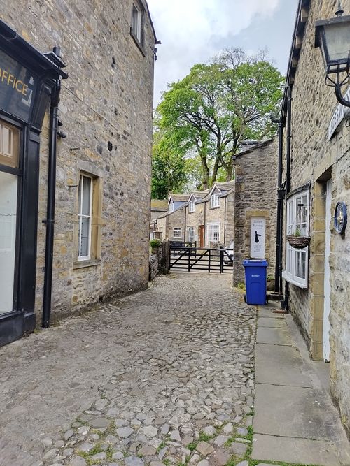 Free Quaint stone alleyway flanked by historic buildings, leading to a leafy residential area. Stock Photo