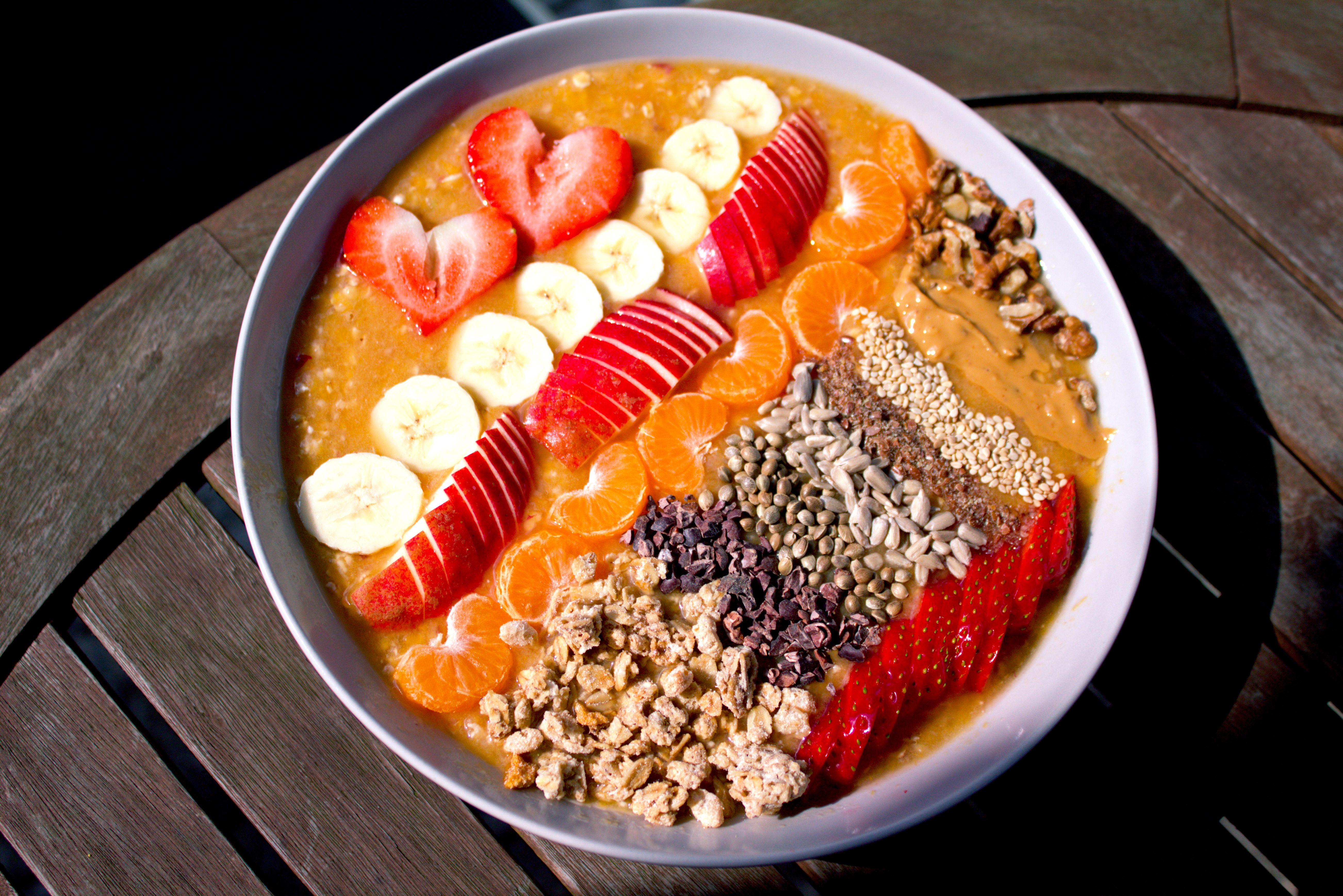 Vibrant smoothie bowl featuring bananas, strawberries, nuts, seeds, and granola with heart-shaped strawberry slices.