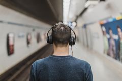 Rear view of a young man listening to music with headphones at a subway platform.