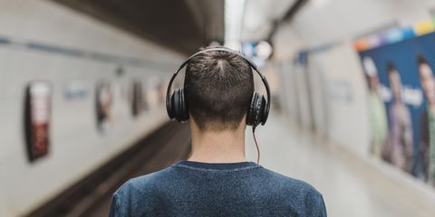 Rear view of a young man listening to music with headphones at a subway platform.