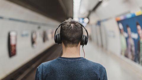 Rear view of a young man listening to music with headphones at a subway platform.