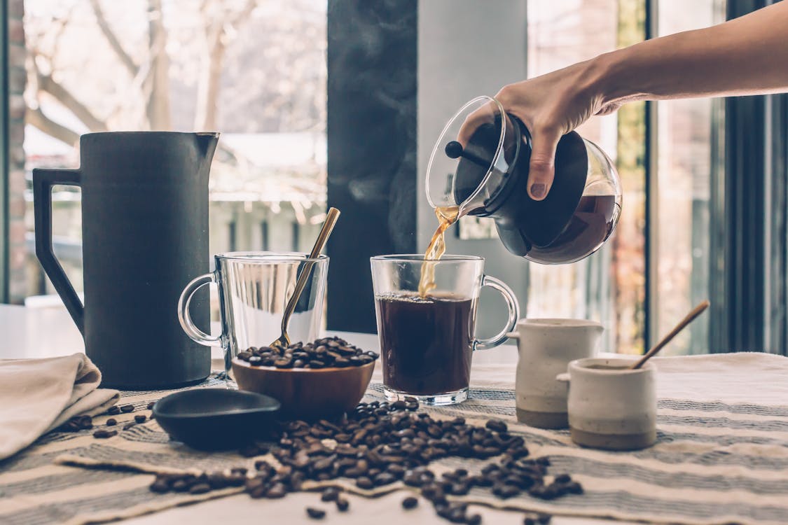 Person Filling Clear Glass Mug With Black Coffee