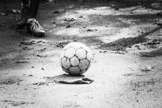 Monochrome image of a soccer ball on a muddy field, with a person's leg visible, suggesting play.
