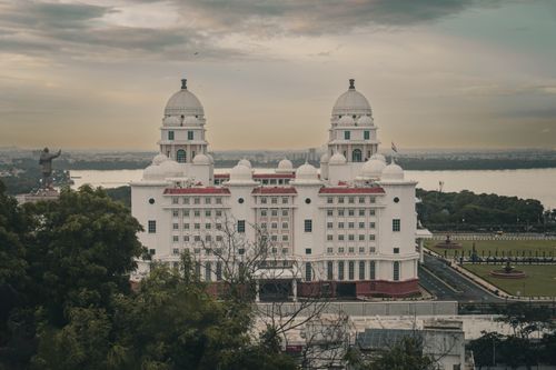 Free A grand white building with domes, surrounded by greenery, overlooking a tranquil river at dusk. Stock Photo