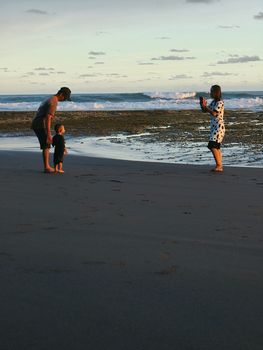 A family capturing memories at the beach during sunset, with waves in the background.