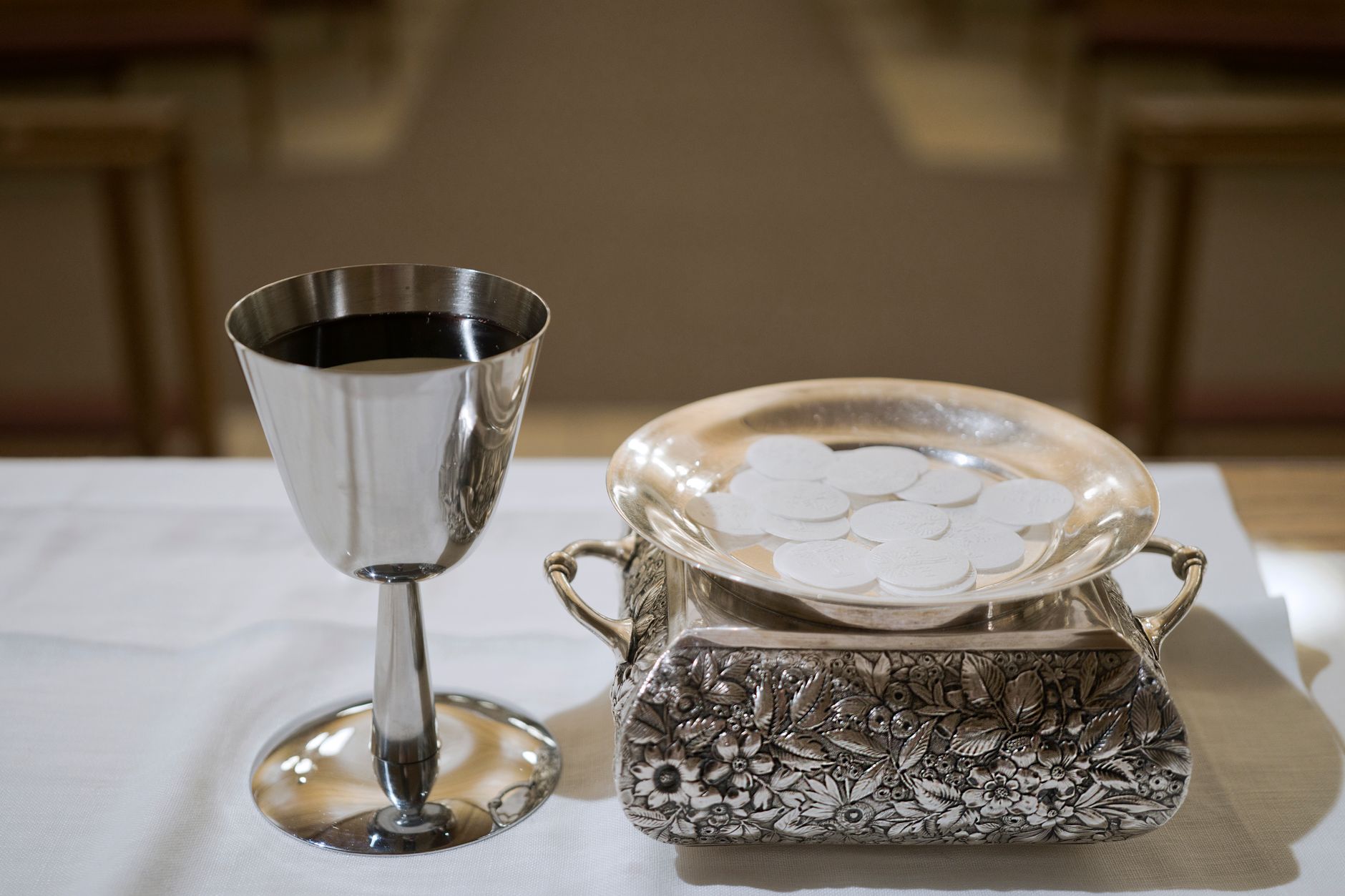 Elegant display of a silver chalice with wine and wafers in a sacred setting, symbolizing the Eucharist.