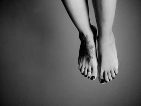 Black and white artistic photo highlighting tattooed feet with dark nail polish.