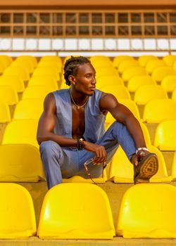 Man in fashionable attire sits in vibrant yellow stadium seats, Ado Ekiti, Nigeria.