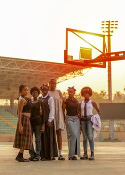 A group of young African women posing together in a stadium during sunset, showcasing vibrant West African fashion.