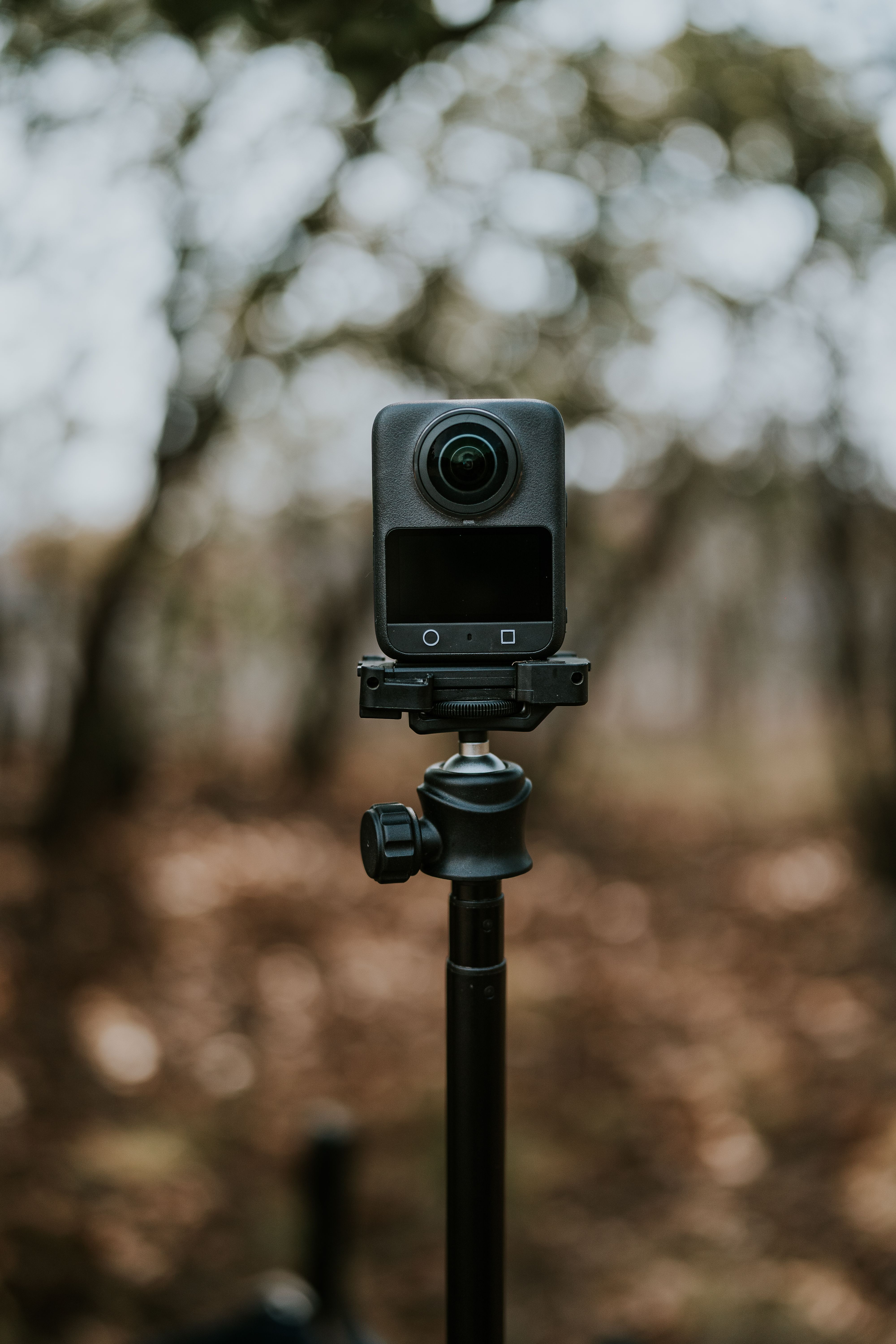 A 360-degree camera mounted on a tripod outdoors in a forested area with blurred background.