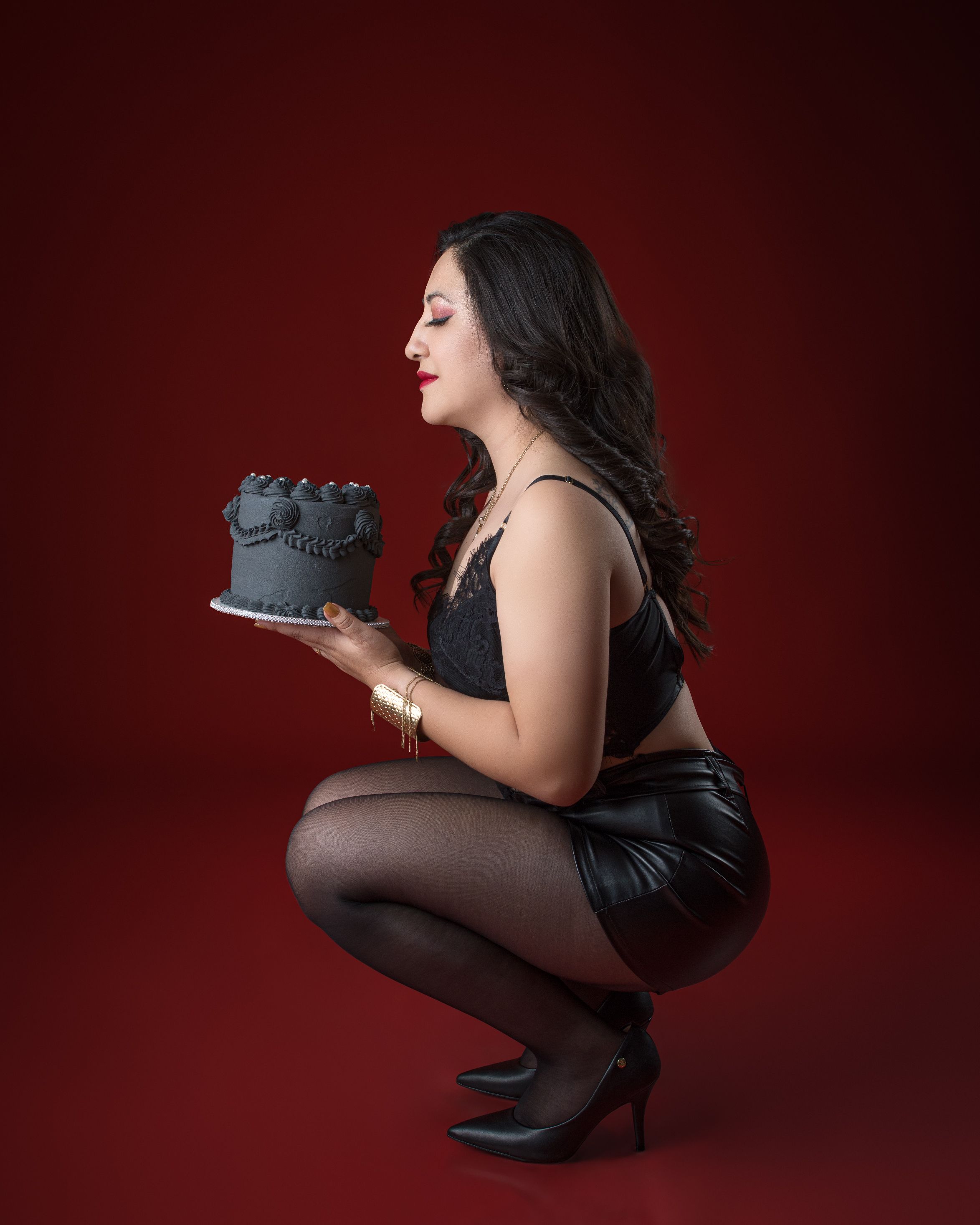 Stylish woman in black holding a decorated cake in a studio setting.