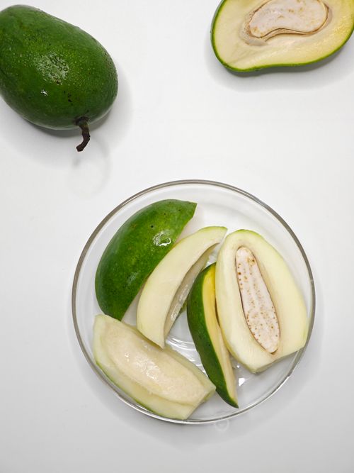 Free Sliced and whole green mangoes are displayed on a white surface. Stock Photo