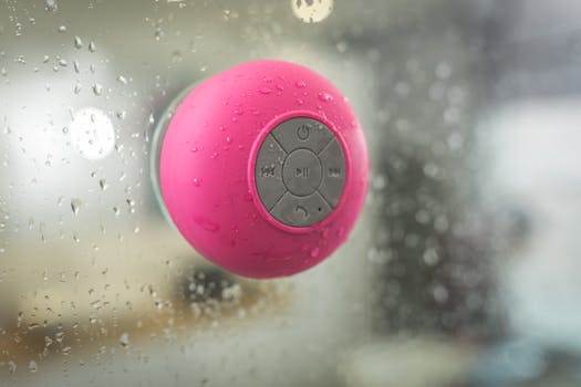 Close-up of a waterproof pink Bluetooth speaker attached to wet glass, showcasing its water-resistant features.