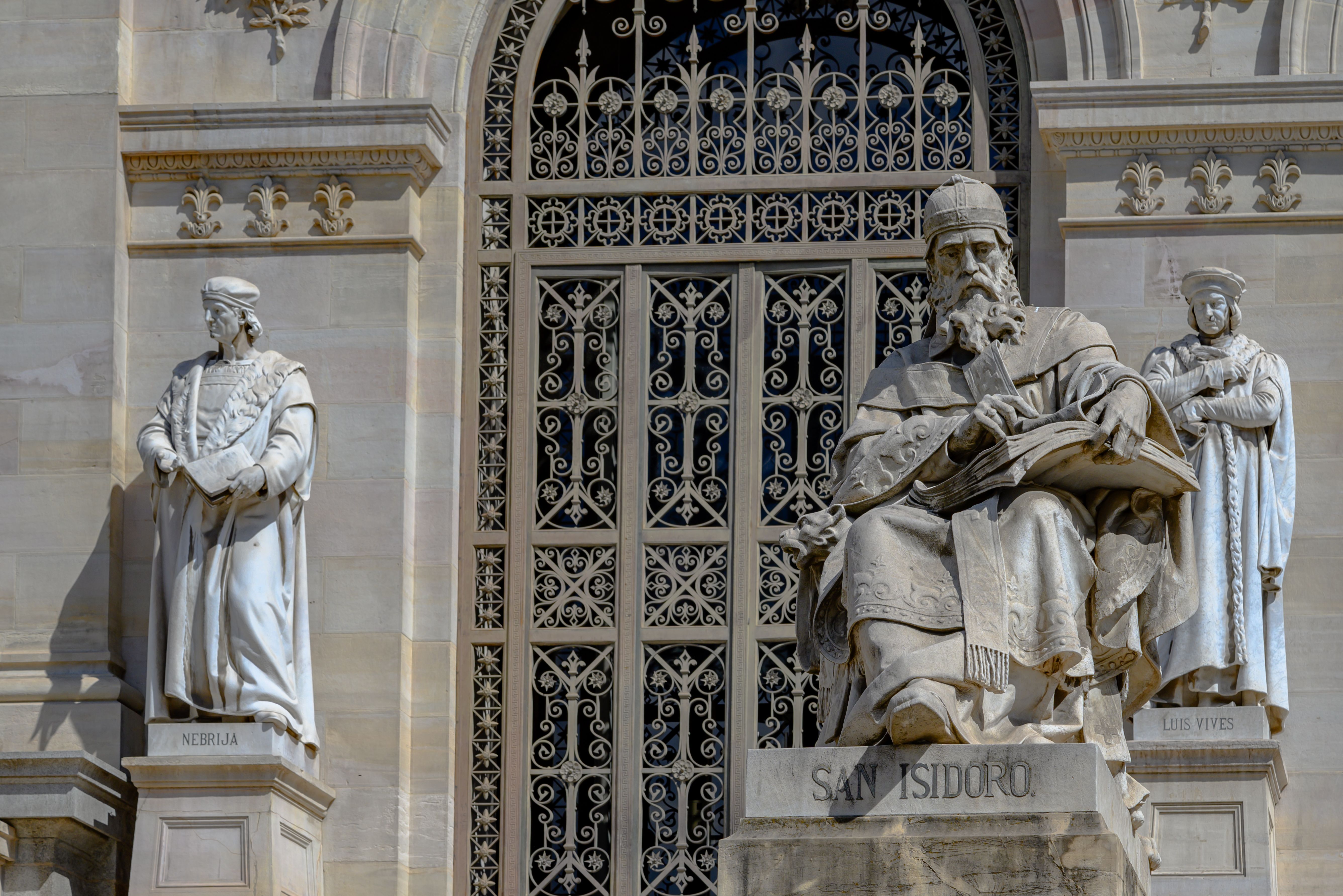 Detailed stone statues of historical scholars at Madrid's Biblioteca Nacional, highlighting ornate architecture.