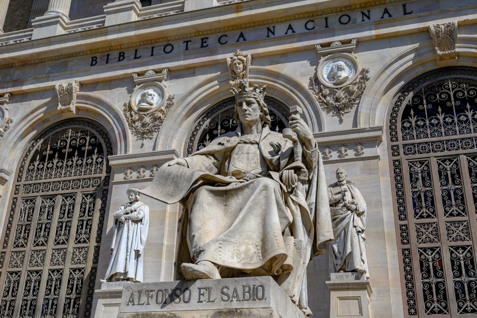 Estatua de Alfonso el Sabio frente a la Biblioteca Nacional en Madrid, España, mostrando arquitectura histórica.