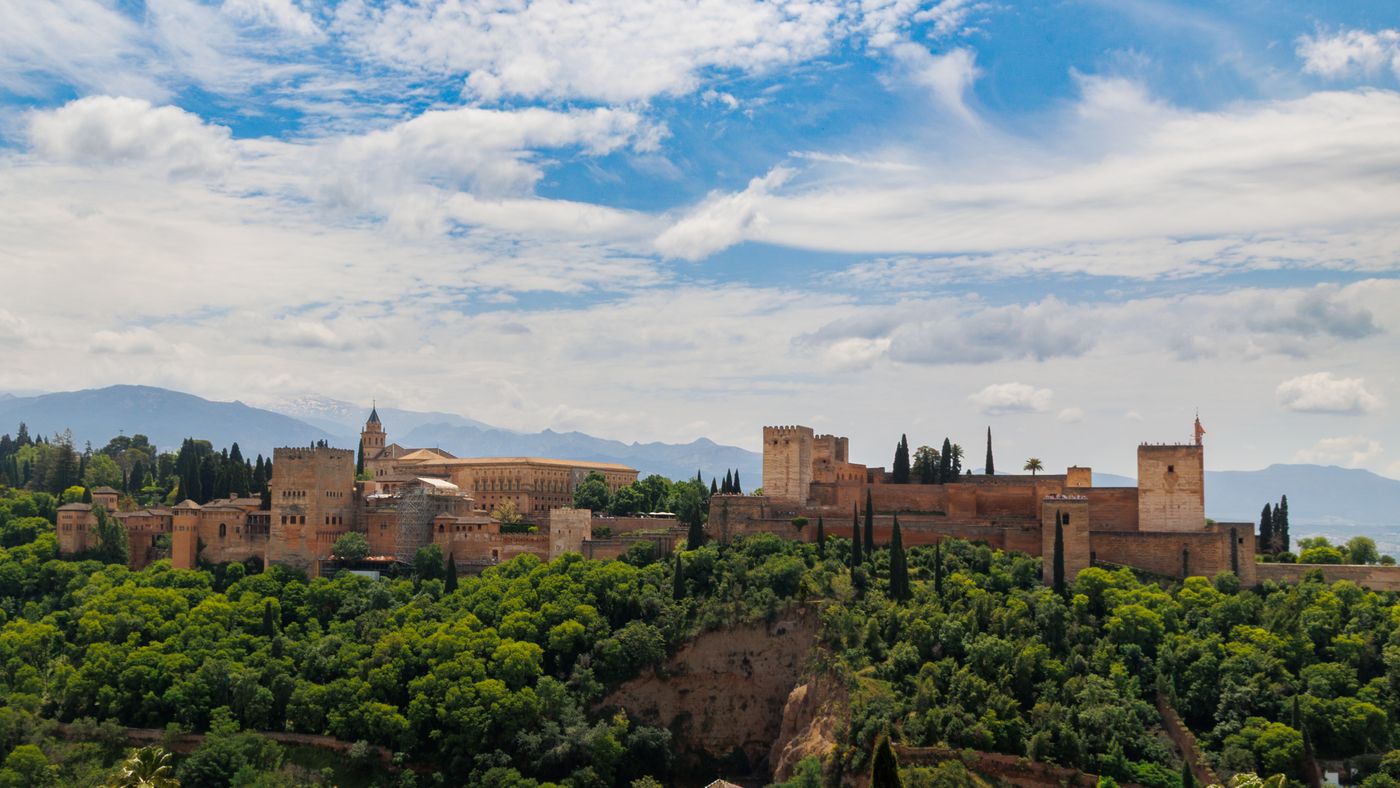The Alhambra palace in Granada among trees under a blue sky