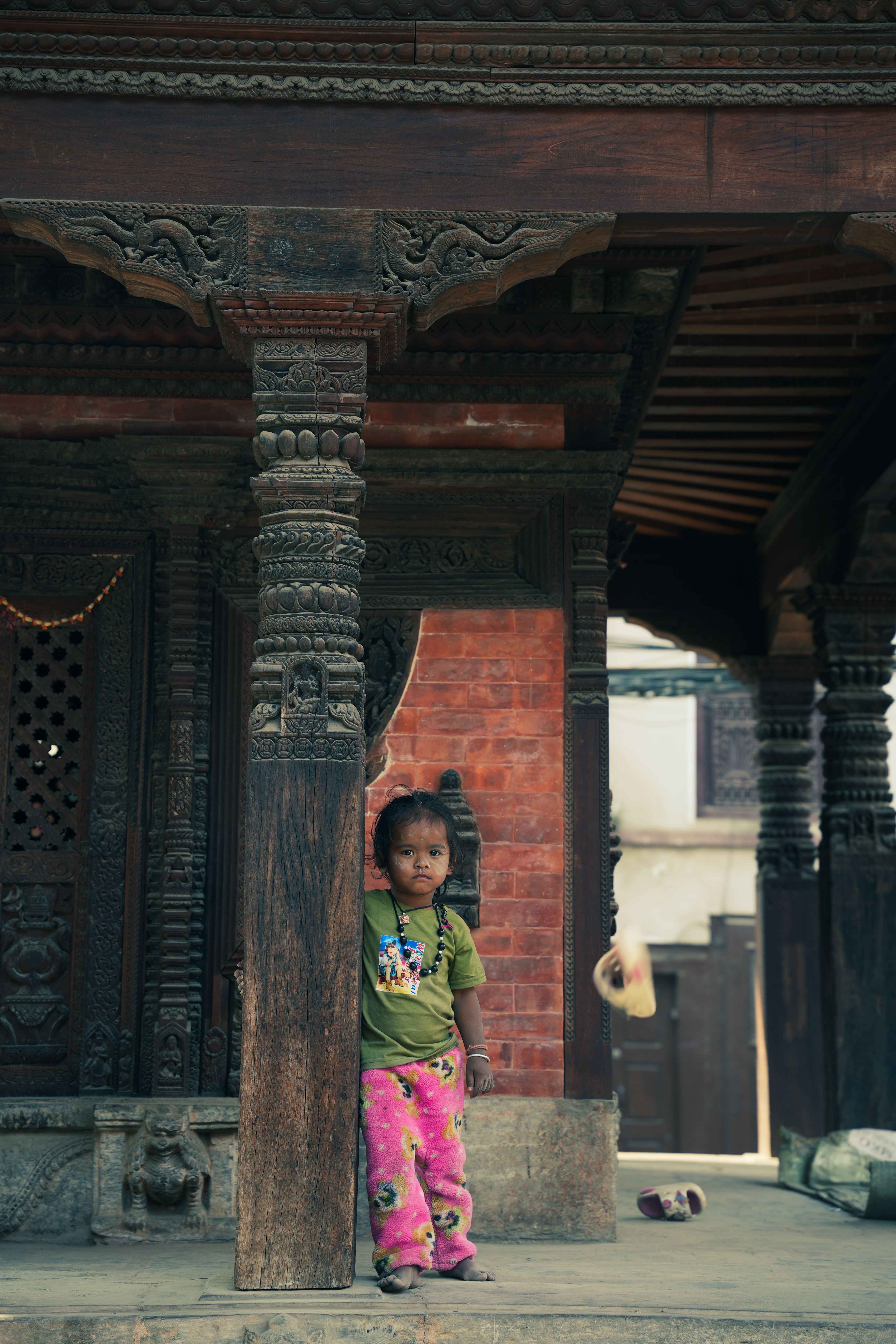 A child stands by intricate wooden columns in Nepal, capturing cultural essence.