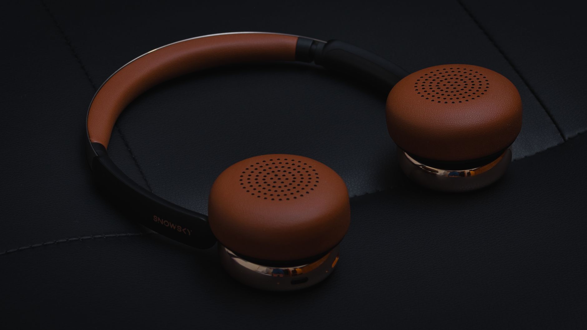 Close-up of stylish brown leather wireless headphones on a black surface, showcasing modern design and elegance.