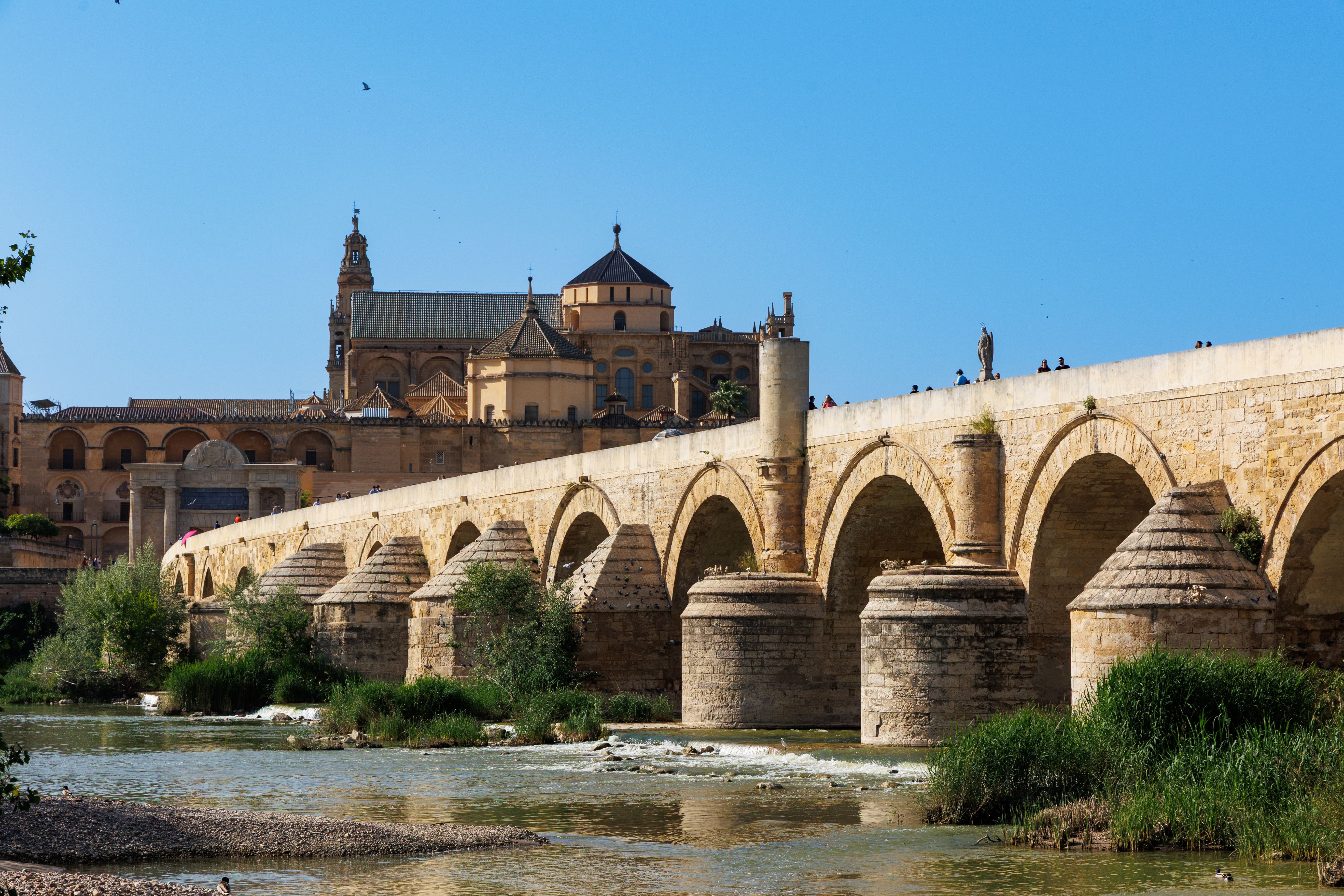 View of the Roman Bridge and Mezquita of Córdoba under a clear blue sky in Andalusia, Spain.