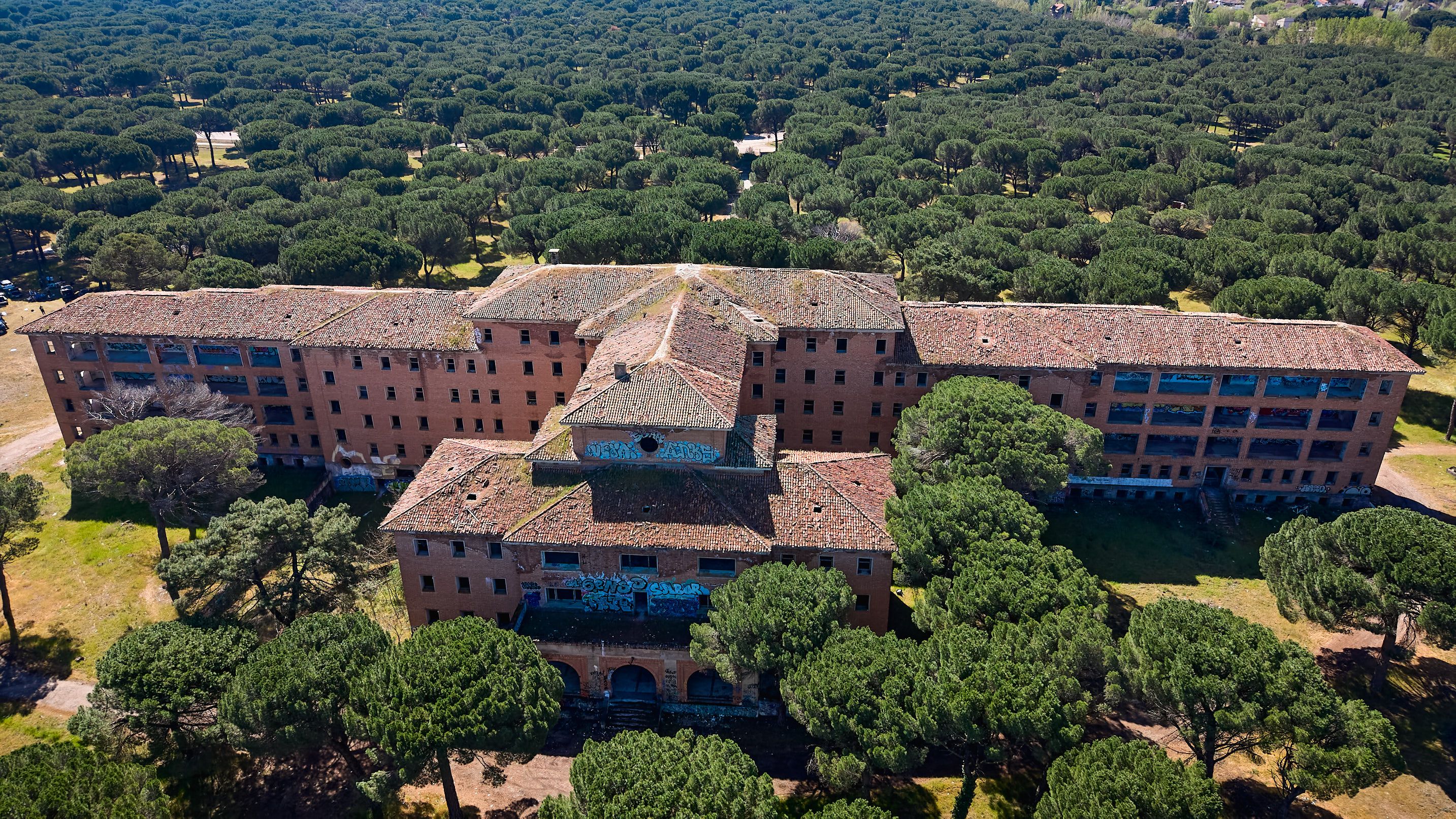 Drone shot of abandoned hospital in Valladolid, surrounded by lush green forest.