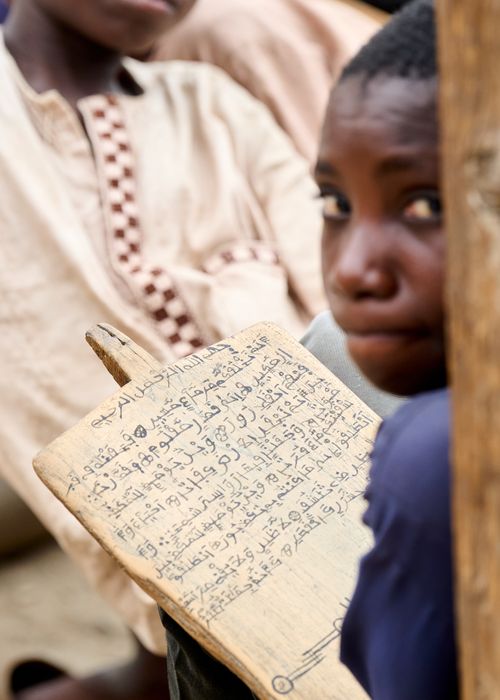 Free A young student studying Arabic script on a wooden board in a traditional classroom setting. Stock Photo