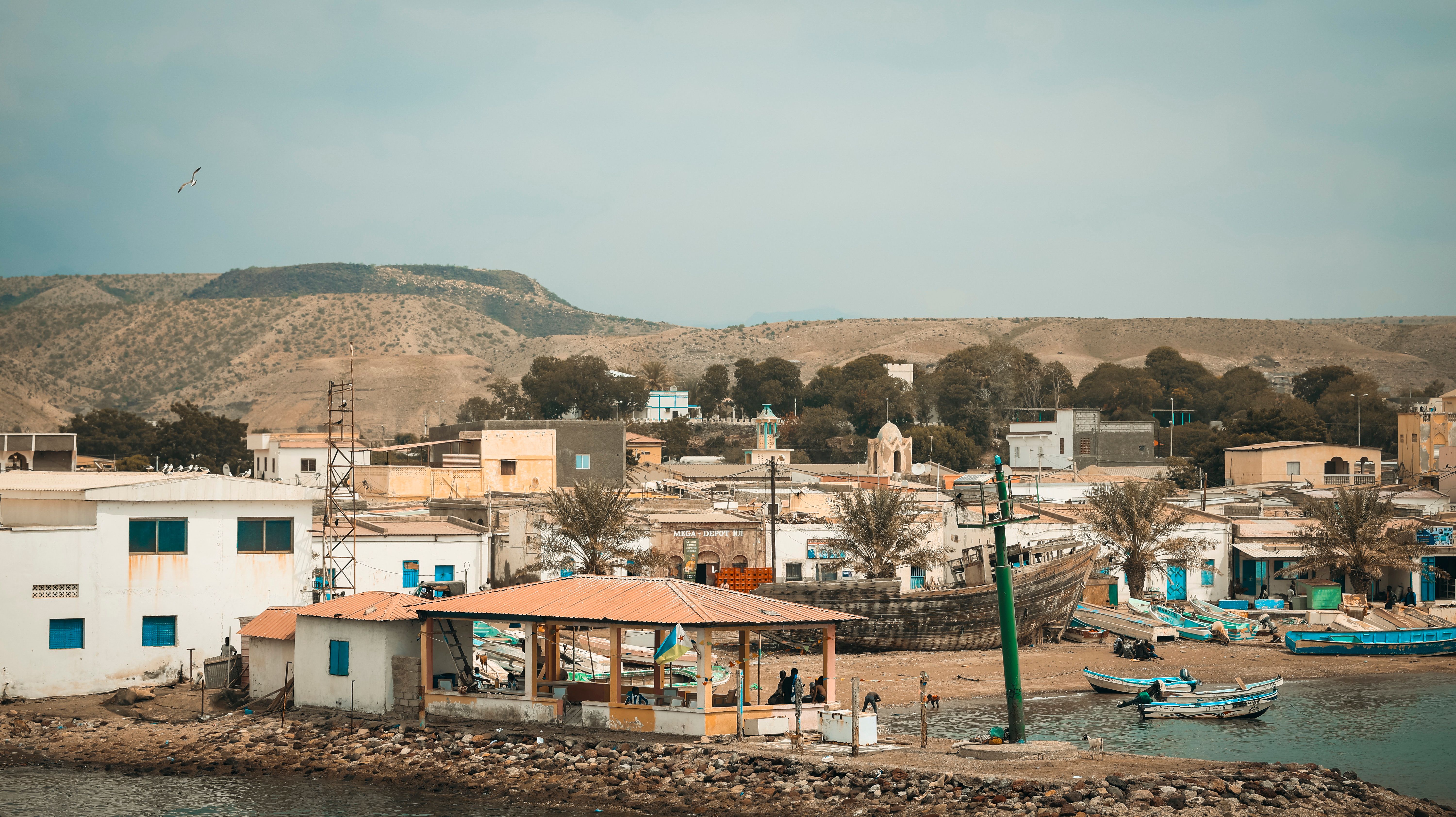 A serene view of Tadjoura's coastal fishing village with boats, buildings, and mountains in Djibouti.