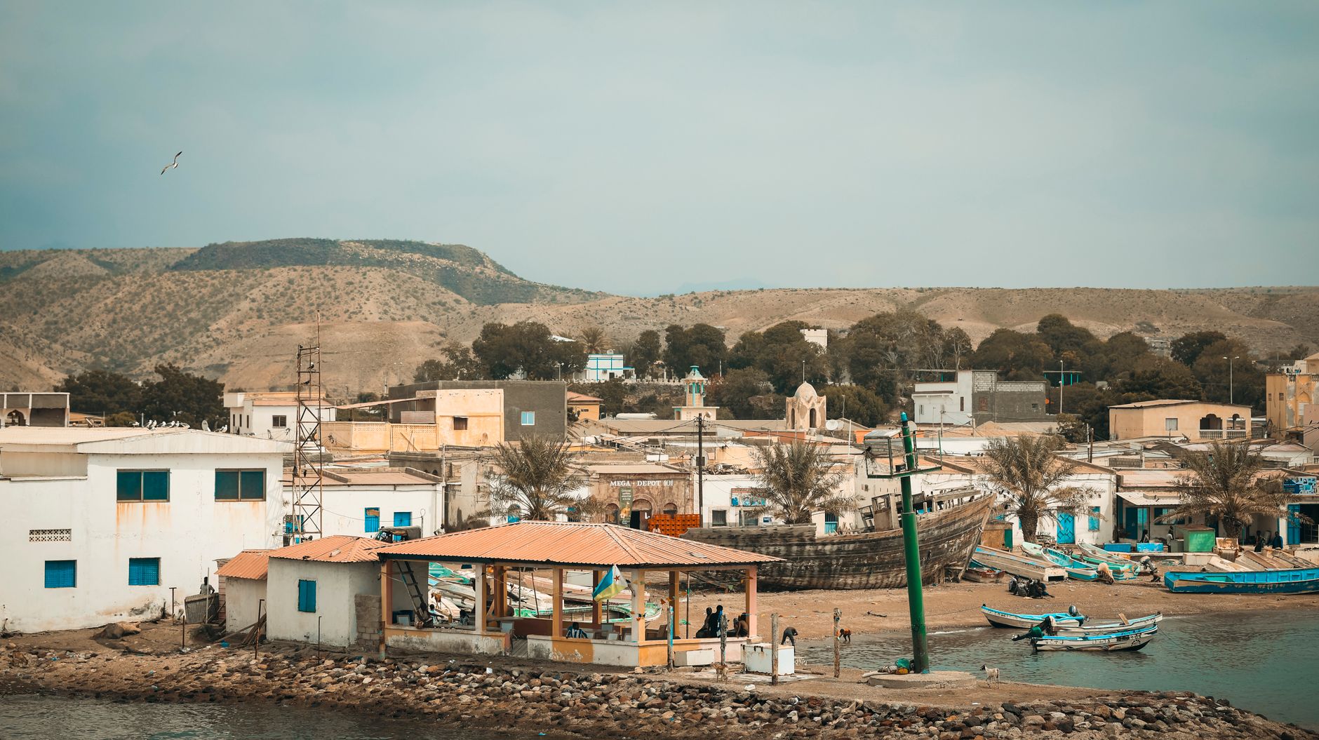 A serene view of Tadjoura's coastal fishing village with boats, buildings, and mountains in Djibouti.