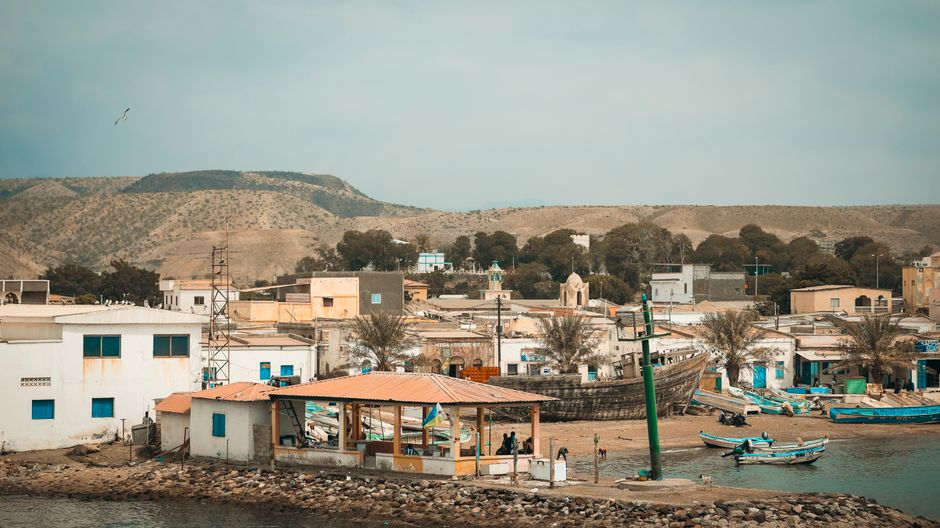 A serene view of Tadjoura's coastal fishing village with boats, buildings, and mountains in Djibouti.