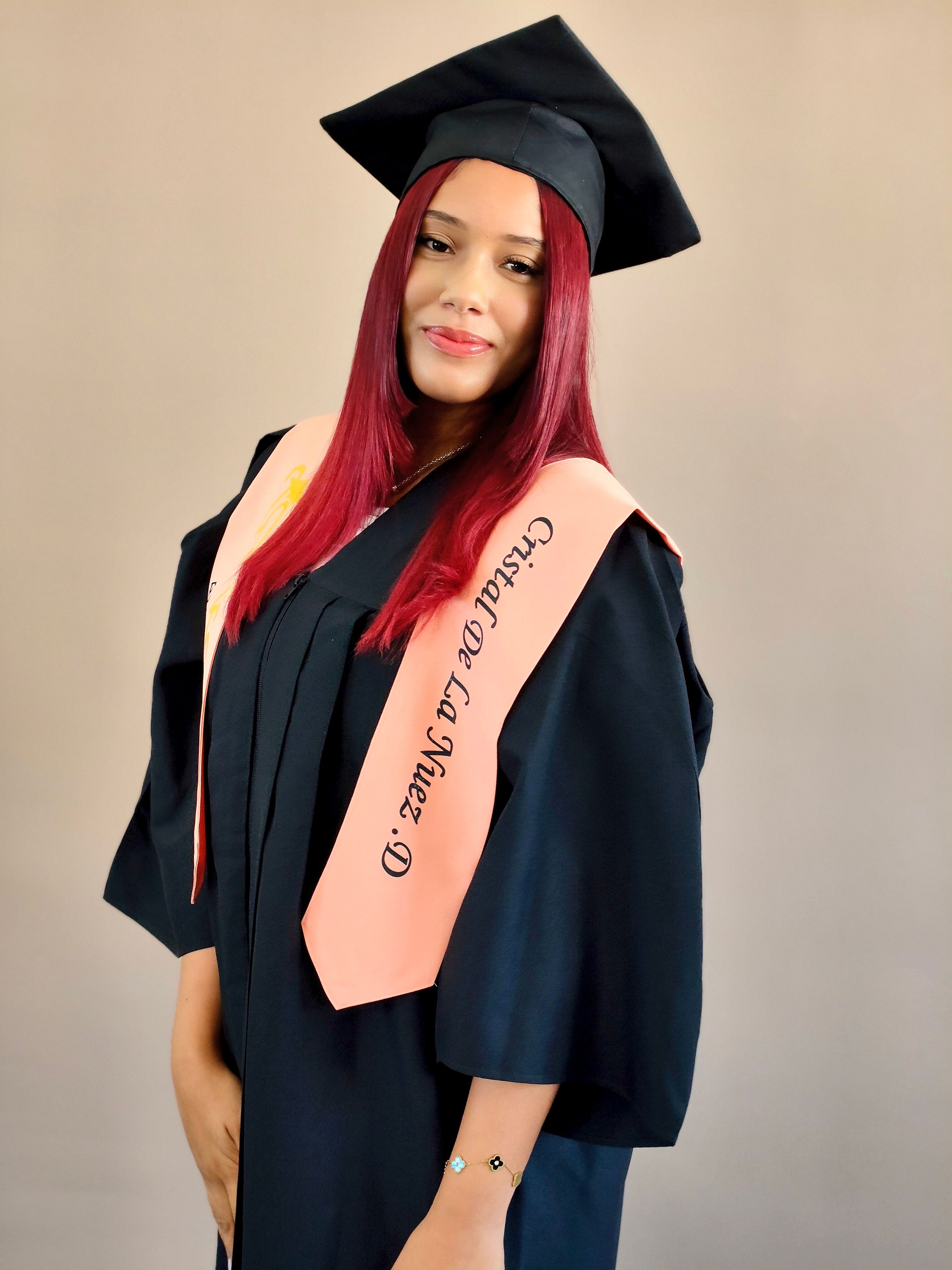 Young woman in graduation gown and cap proudly posing with diploma sash.