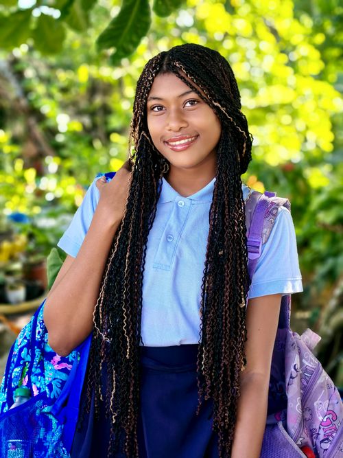 Free Teen girl with braided hair stands in a garden carrying colorful backpacks. Stock Photo
