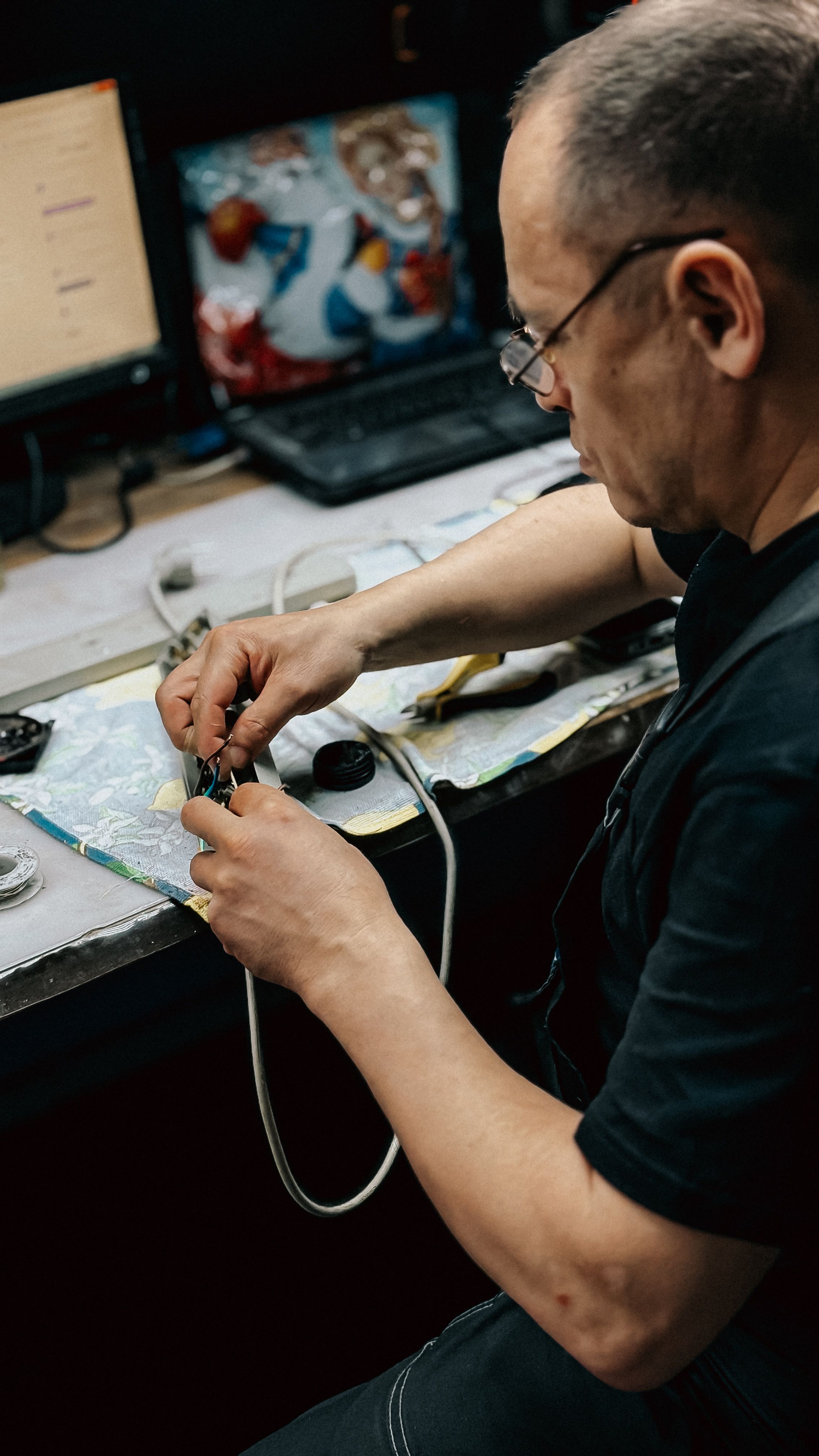 Technician focused on repairing electronic device at a cluttered desk with tools and components.