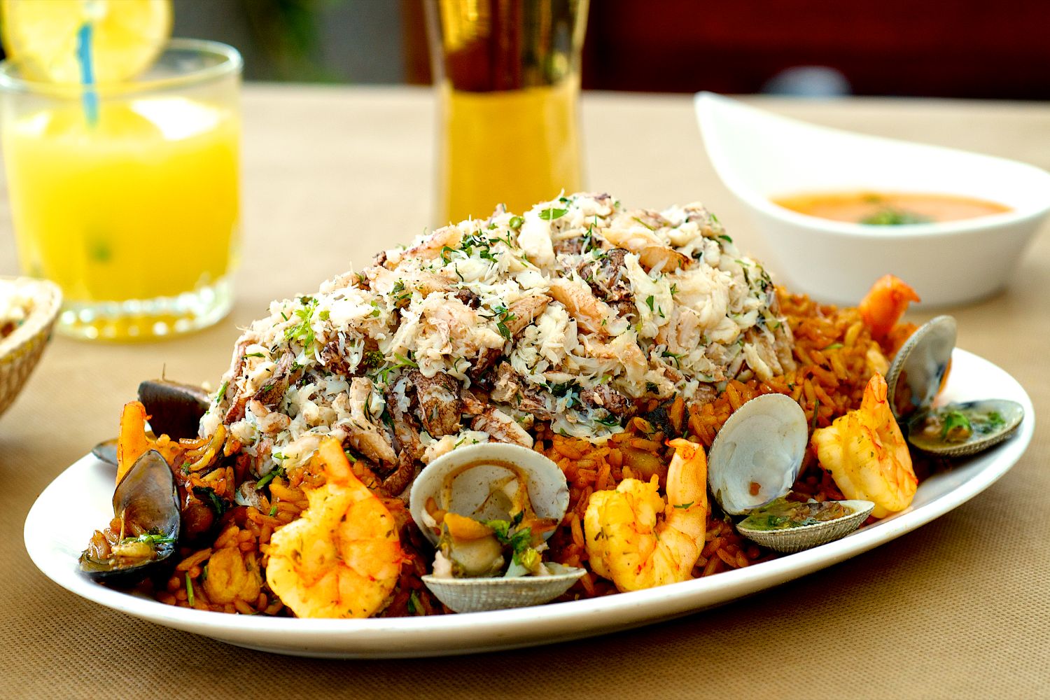 Saffron-red seafood paella rice piled with large shrimp, opened clams and mussels, generous white crab meat, chopped parsley, and lemon nearby