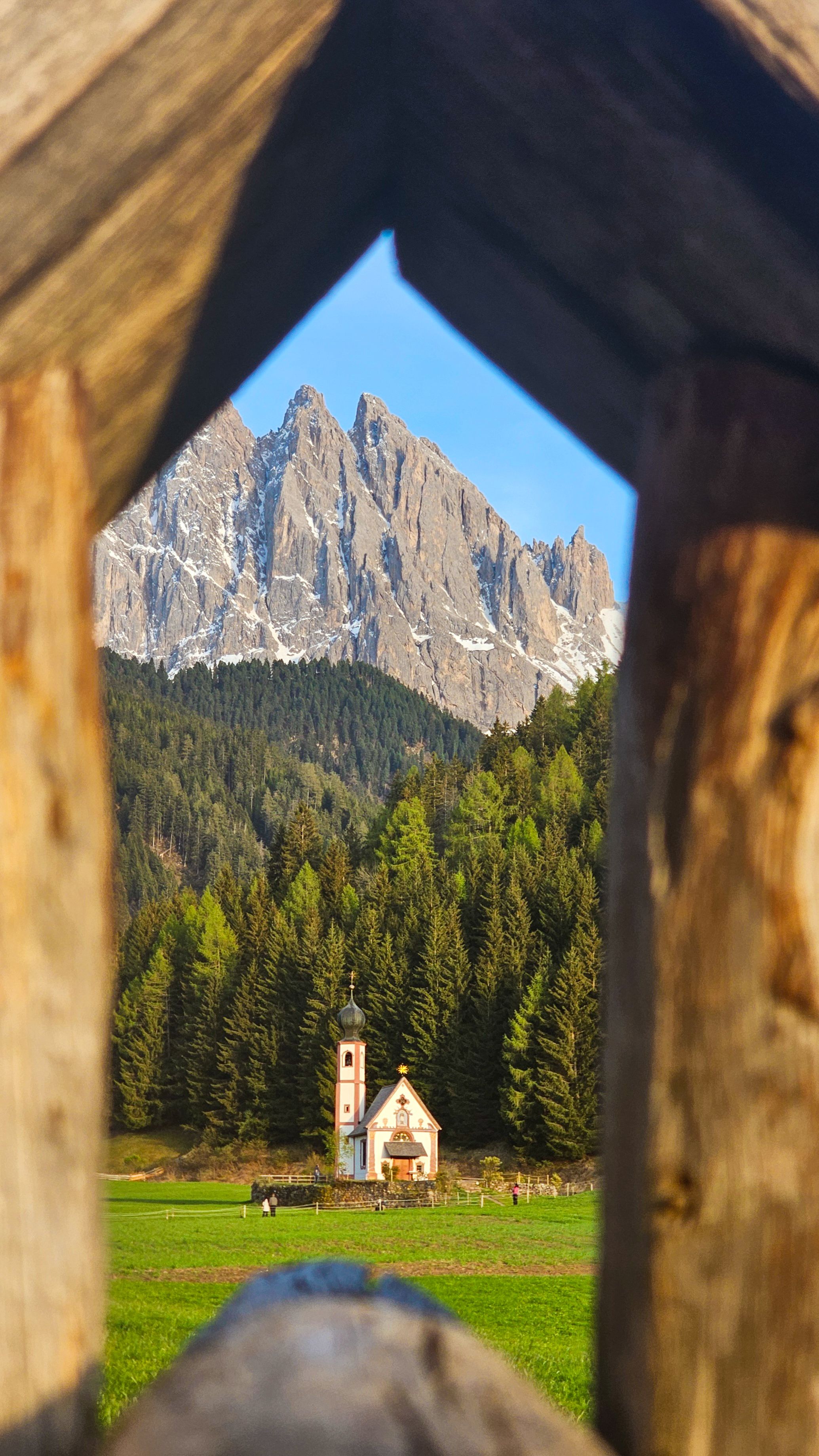 A charming rural church nestled in a forested valley, framed by a distinctive mountain peak.