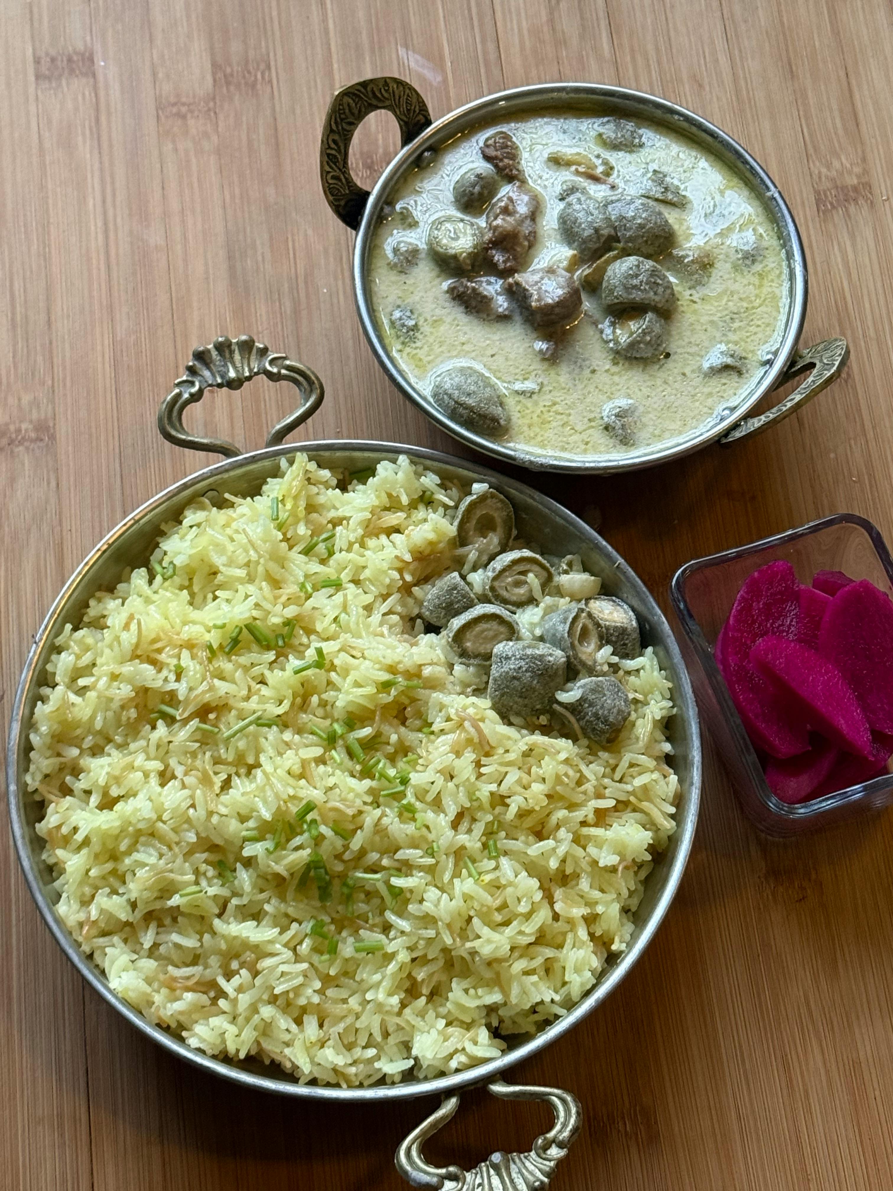 A traditional Middle Eastern Mansaf with rice, sauce, and pickled radishes on a wooden table.