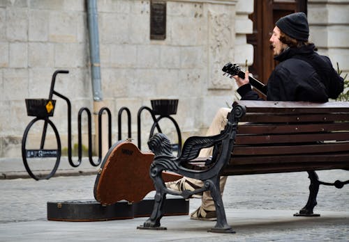 無料 茶色の木製のベンチに座っている黒いスーツの男 写真素材