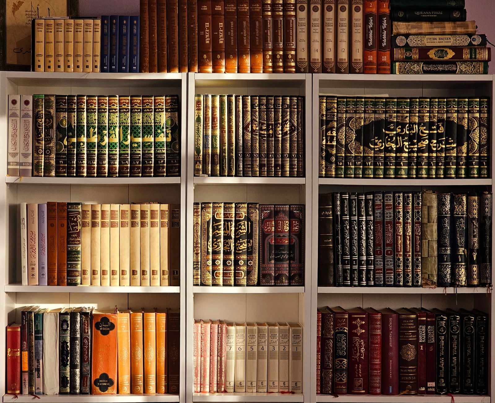 A collection of Arabic language books neatly arranged on a wooden library shelf.