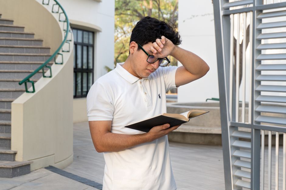 A young man in a white polo reads a book outdoors in a modern setting in Piura, Peru. A young man in a white polo reads a book outdoors in a modern setting in Piura, Peru.