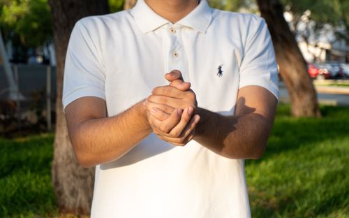 Free Close-up of a man clapping his hands together in a sunlit park in Piura, Peru, wearing a white polo shirt. Stock Photo