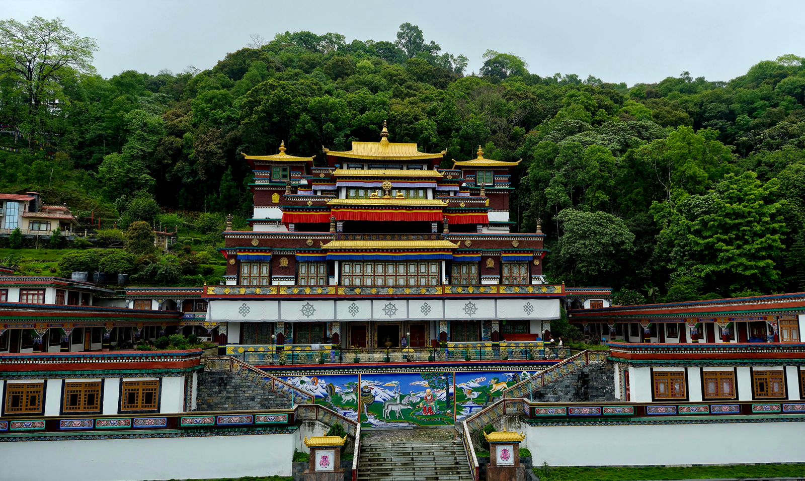 Lingdum Monastery in Sikkim, its gold roofs and white walls rising in tiers above a painted stair and forest