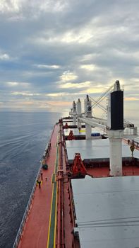 A large cargo ship sails through the ocean under a cloudy sky, creating a serene maritime scene.