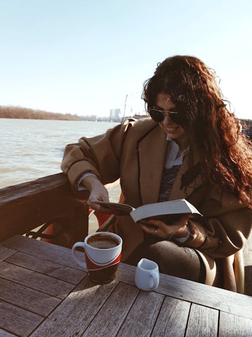 Free Woman in Brown Coat Sitting on Brown Wooden Dock Stock Photo