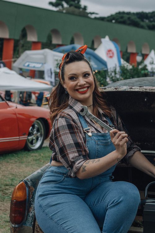 Free Cheerful woman in vintage attire holding a wrench at an outdoor car show. Stock Photo