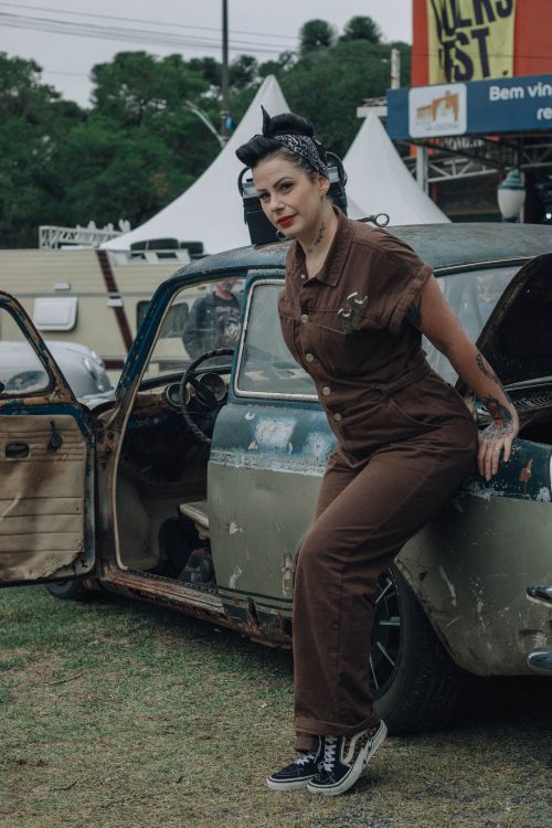 Free Woman dressed in vintage style leaning against a classic car at an outdoor event. Stock Photo