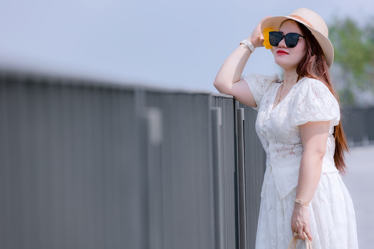 a fashionable woman in a white dress and sun hat posing outdoors with
