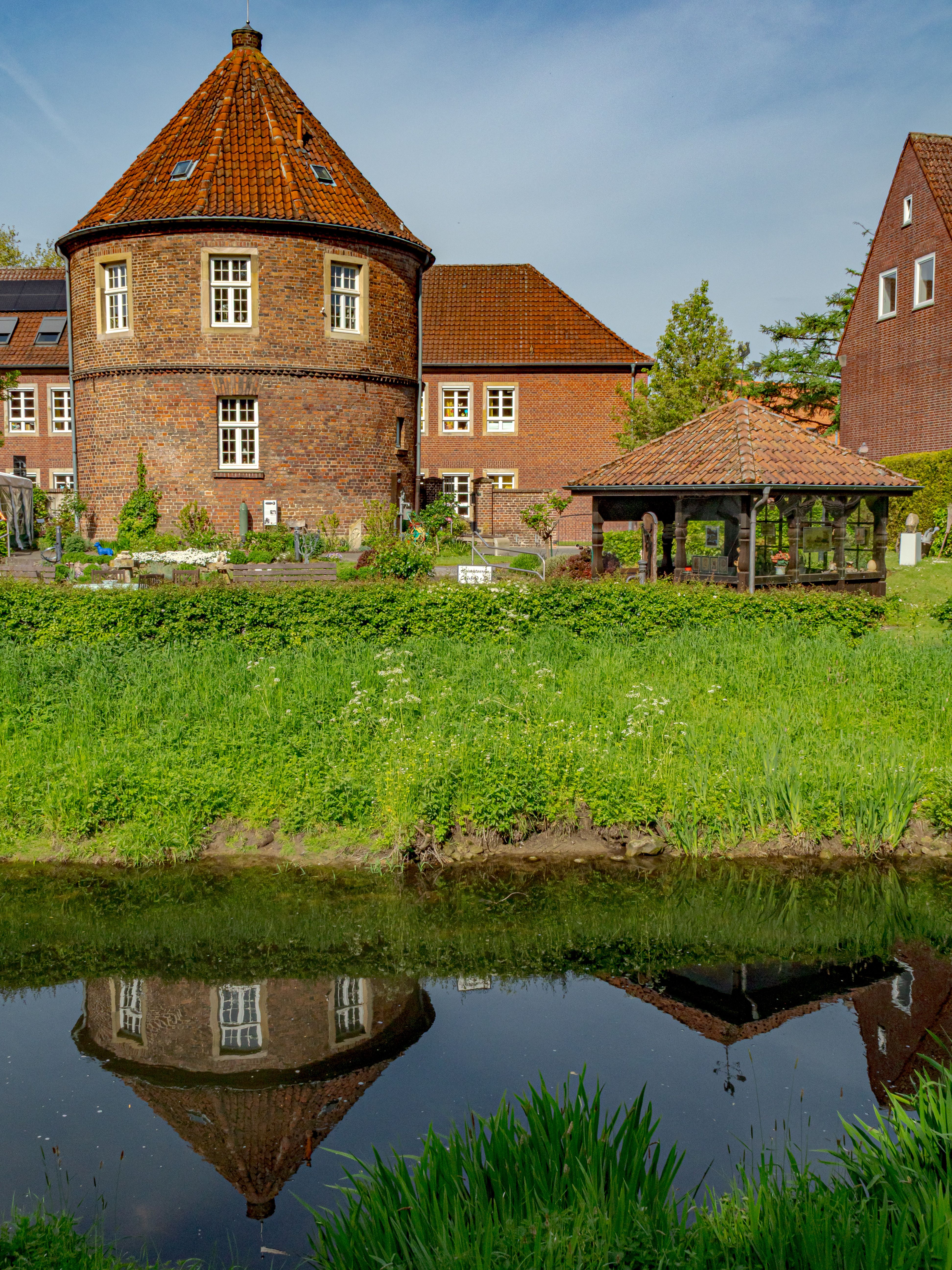 Charming historic brick building in Coesfeld, Germany with beautiful pond reflection and vibrant greenery.