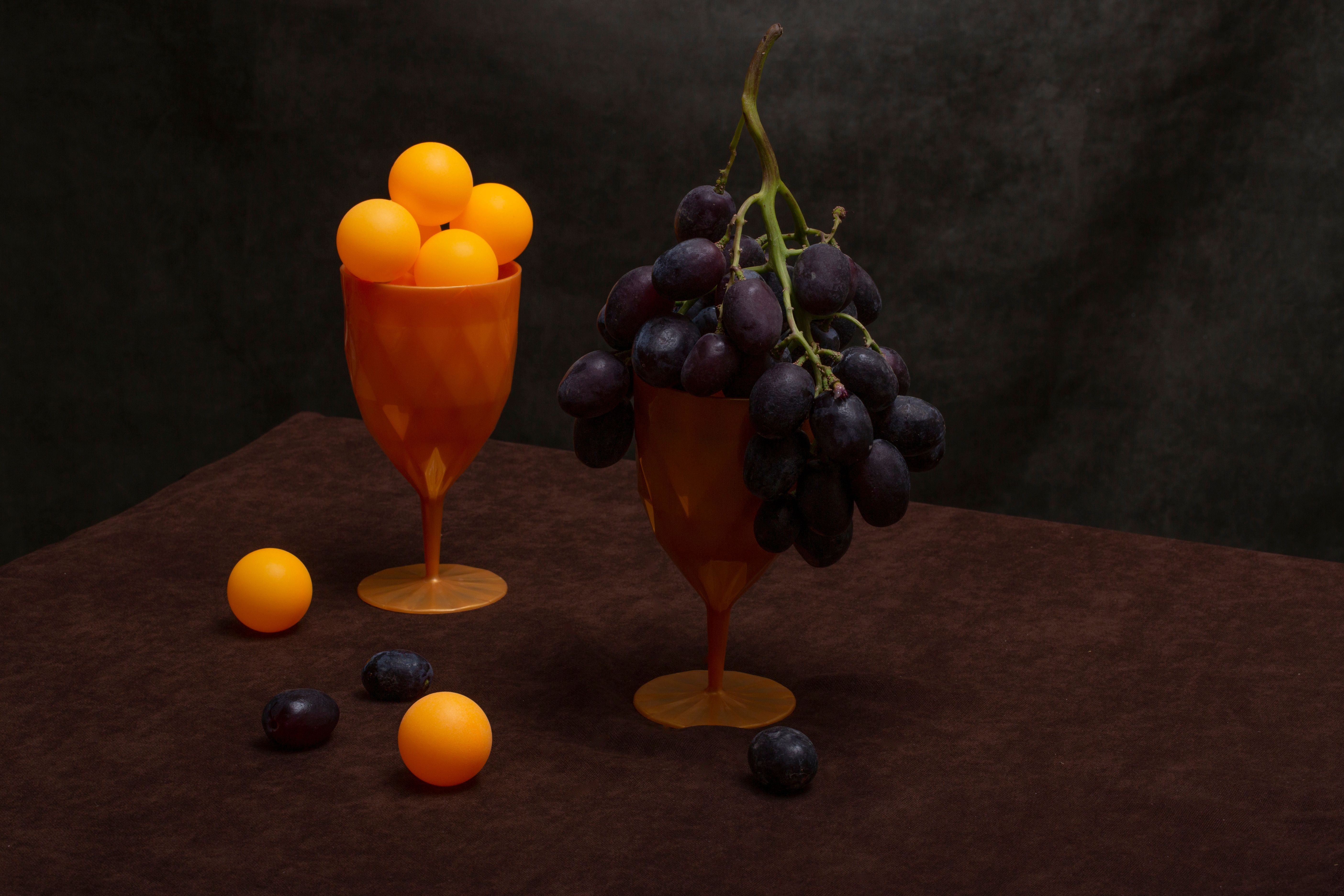 A creative still life composition featuring grapes and orange balls in polygonal orange glasses.