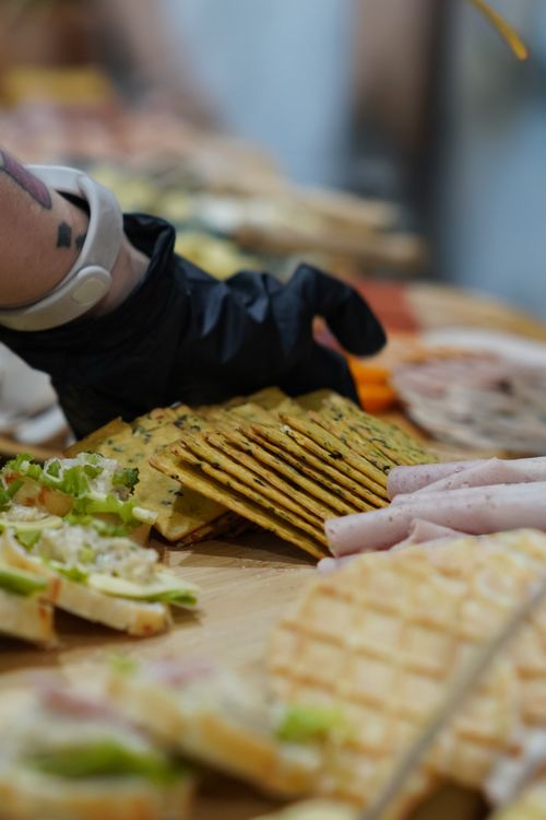 Free Close-up of a hand in a glove serving a variety of tasty gourmet appetizers on a wooden table. Stock Photo