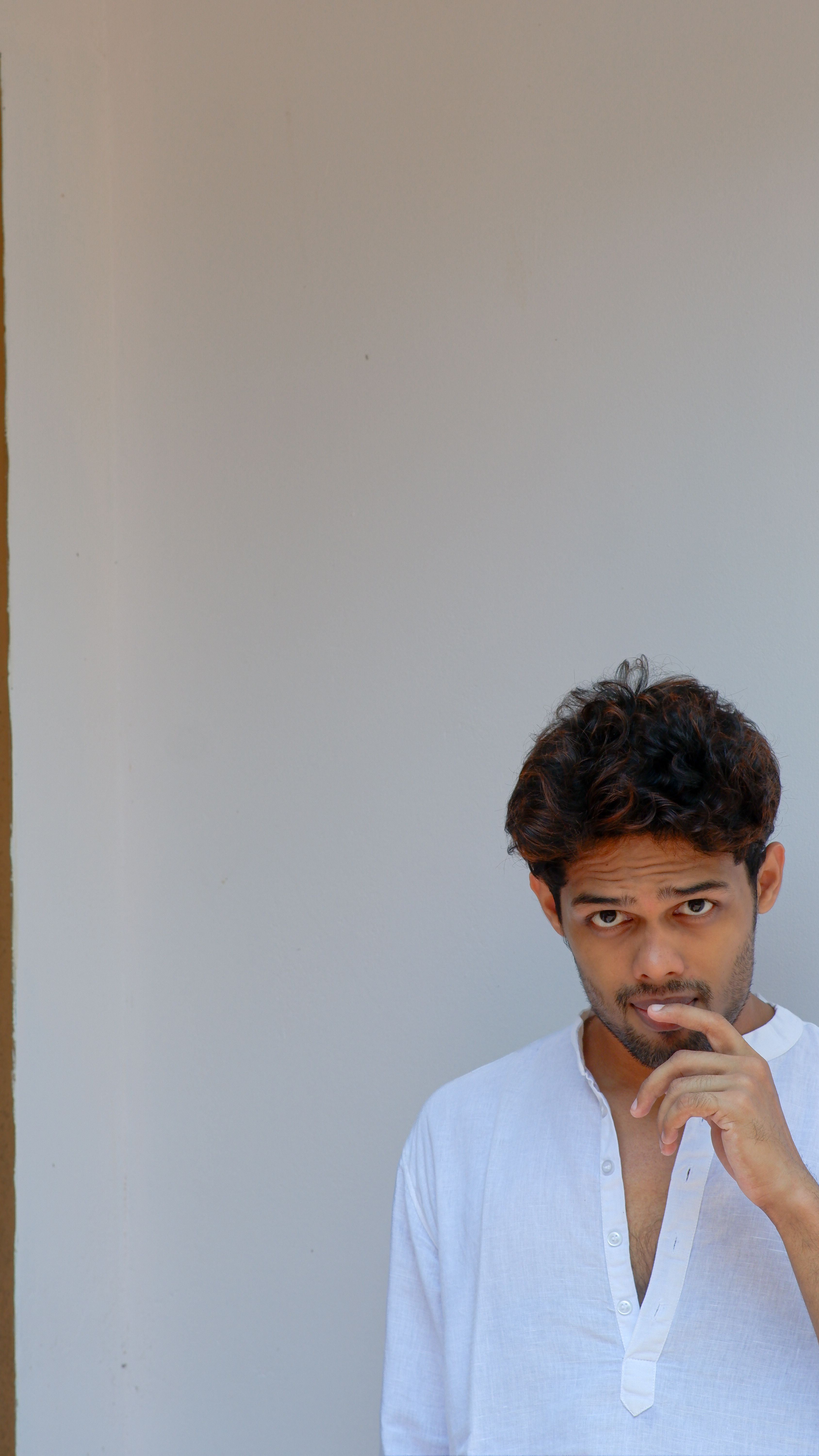 Serene portrait of a man in a white shirt against a minimalist white wall.