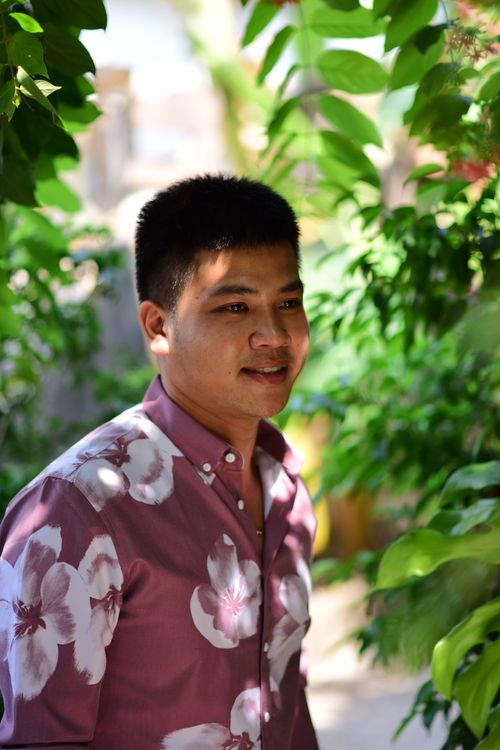 Free Casual portrait of a young man in a floral shirt, surrounded by lush green foliage, exuding a relaxed vibe. Stock Photo