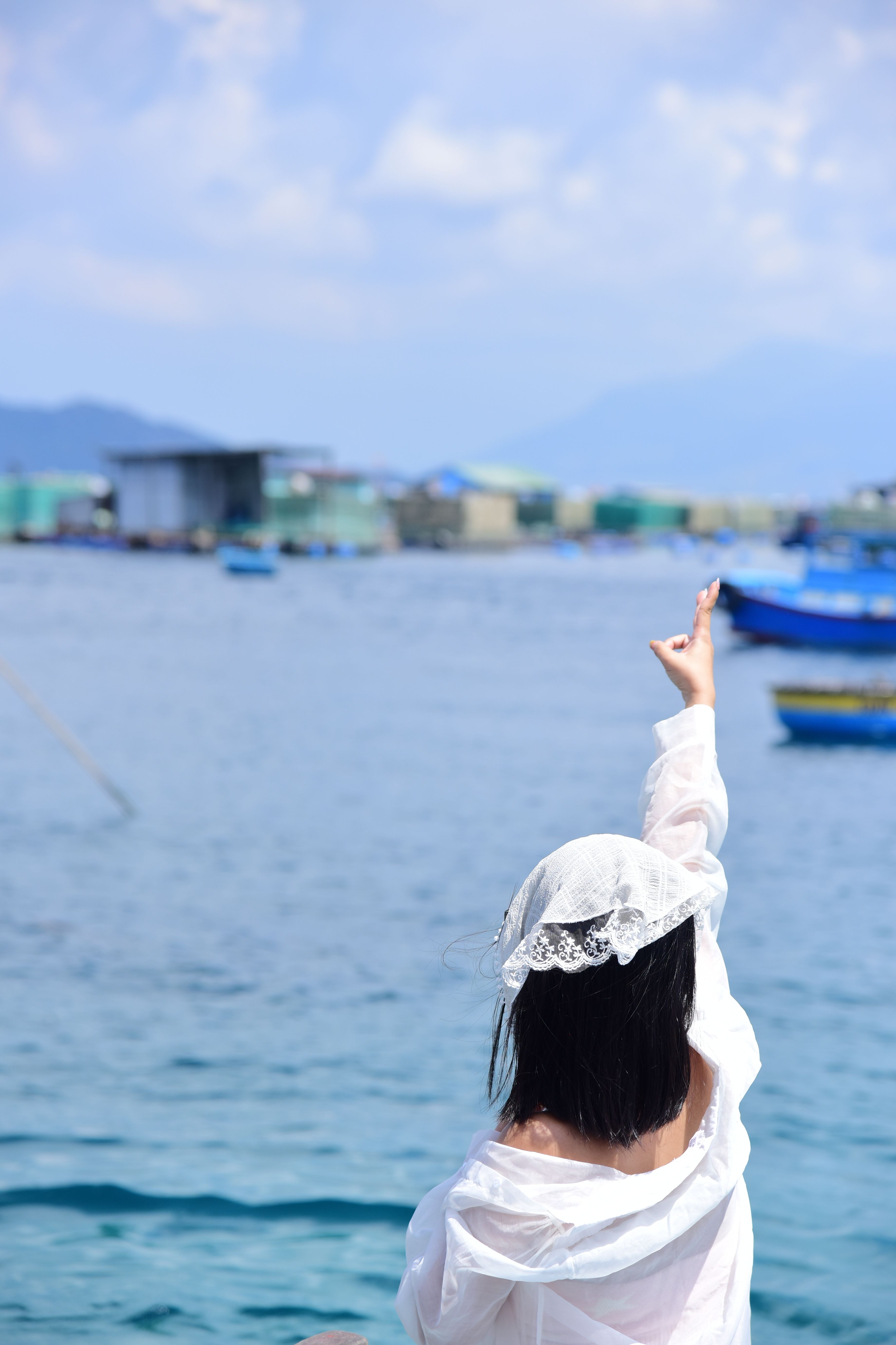 A woman in white gestures toward the sea, capturing a serene coastal moment.